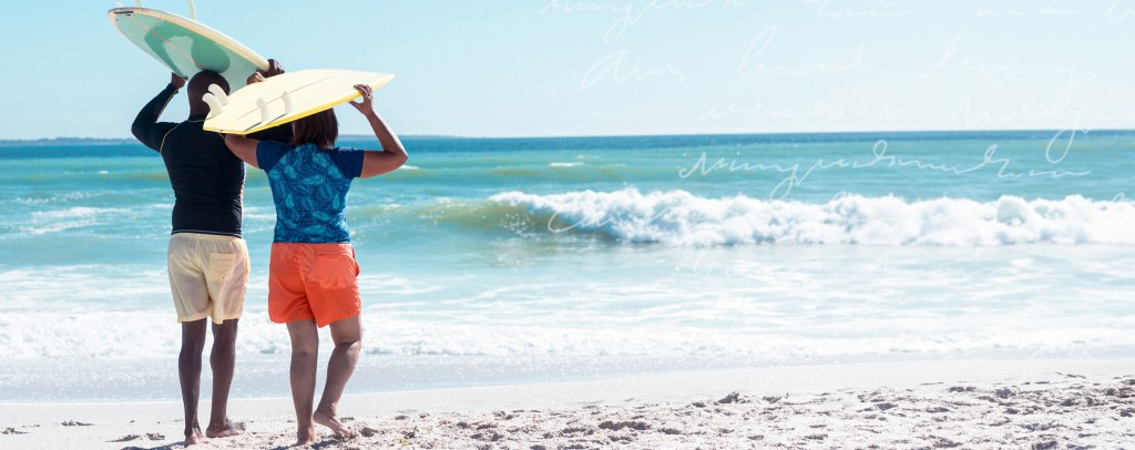 Couple walking towards the ocean with surfboards over their heads