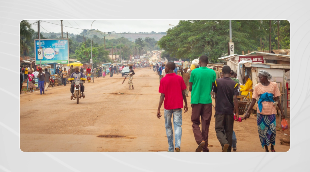 City street in Bangui, Central African Republic, filled with people walking and vehicles traveling down the road.