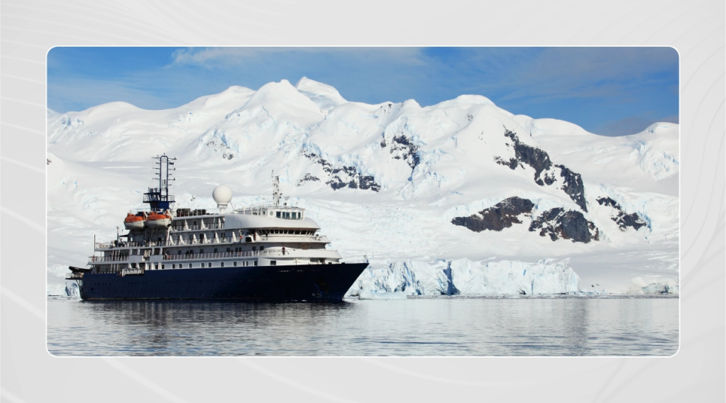 Small cruise ship sailing through the Antarctic with snowcapped mountains and icecaps in the background.