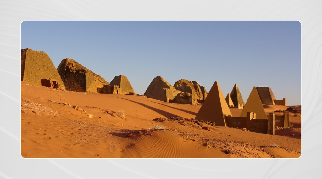 Pyramids of Meroe in the Sudan with a pale blue sky contrasting the tones of the sand and pyramids.