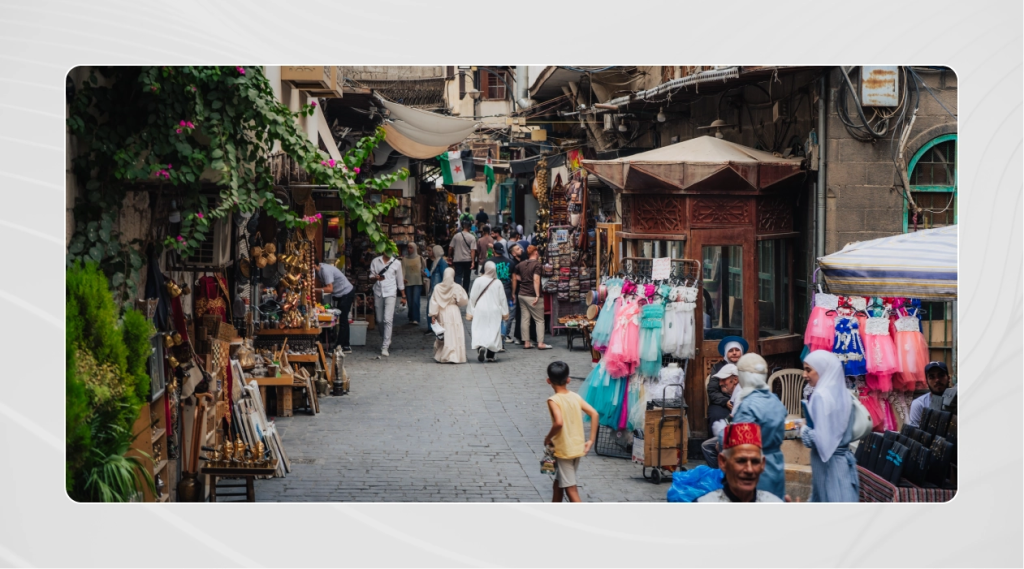 Crowds walk through Souk al-Khayyatin, the historic tailors’ market in the Old City of Damascus, lined with shops selling textiles, clothing, and traditional goods.